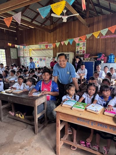 Mr. Sytha Nan, founder of REEC, with schoolchildren holding their new books in a rural classroom